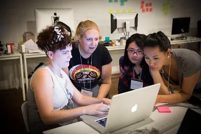 Four women laughing together at a laptop