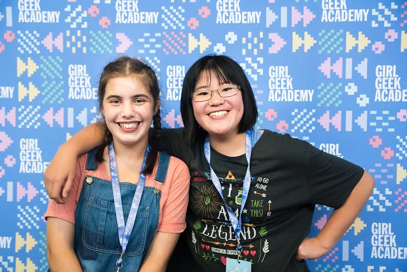 Two girls smiling in front of a Girl Geek Academy backdrop