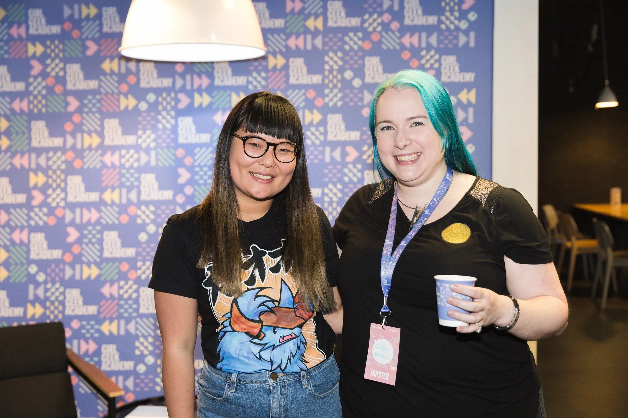 Two girl geeks smiling in front of a patterned wall