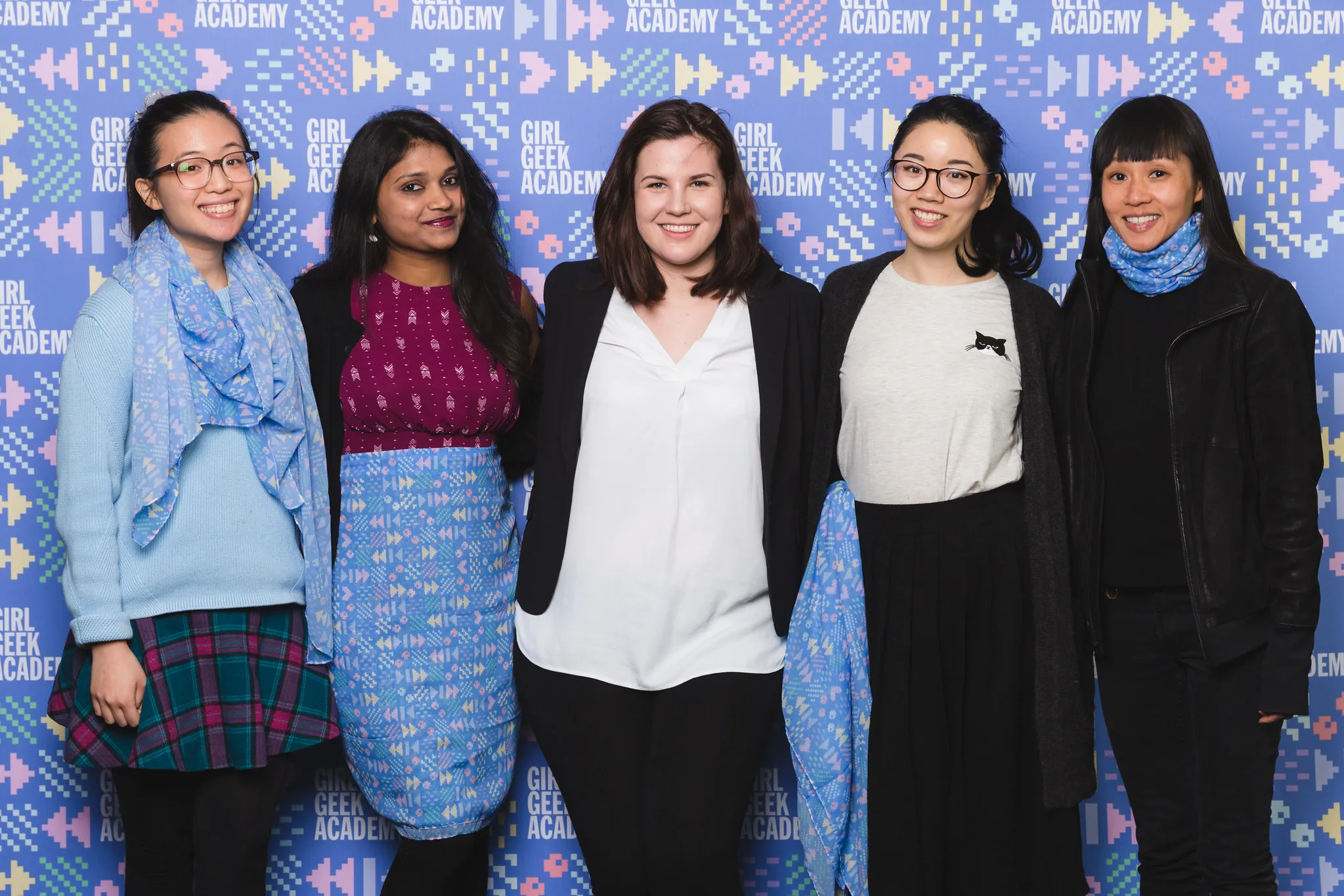 A team of five taking part in #SheHacks, in front of a patterned wall
