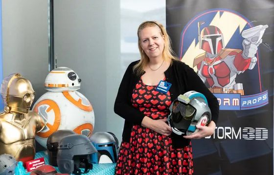 April Staines holding a pilot helmet beside her 3D-printed droids and props