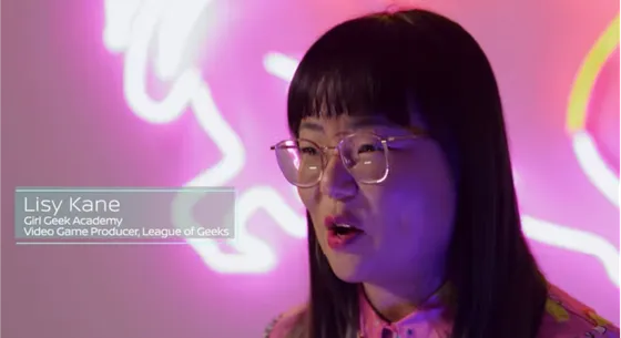 Lisy Kane speaking on camera in front of a neon sign