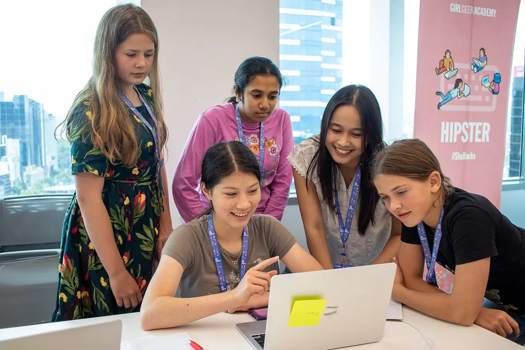 A student points at her laptop screen while four others lean in to look