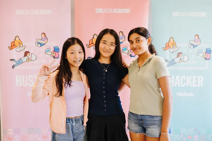 Three students posing in front of Girl Geek Academy banners